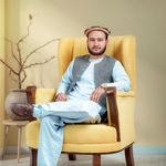 Man in traditional attire sitting in a yellow armchair indoors, exuding relaxation and confidence.