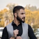 Portrait of a fashionable bearded man outdoors, adjusting his watch in formal attire.